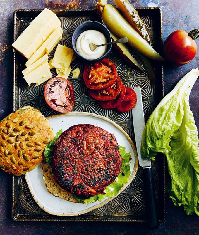 best burger recipes: beet veggie burger on a plate, surrounded by toppings and a seeded bun