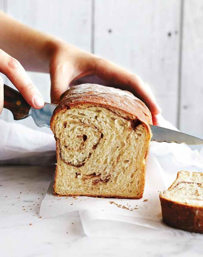 fun things to bake: front end of a sliced no-knead cinnamon swirl bread with a hand slicing into it with a knife