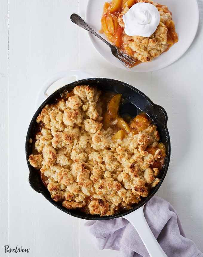 fun things to bake: aerial of skillet peach cobbler with a scoop missing, next to a plate with peach cobbler topped with whipped cream