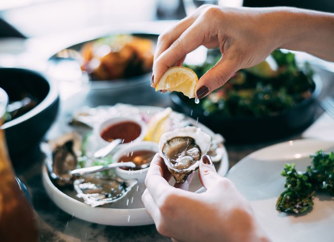 how to shuck oysters: someone spritzing lemon wedge atop a raw oyster