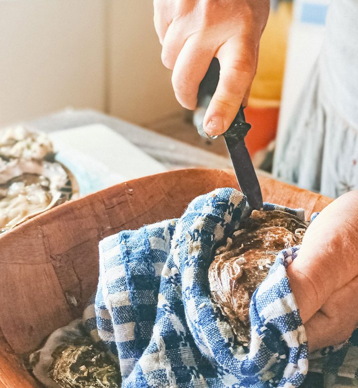 how to shuck oysters: hands shucking oysters in a kitchen