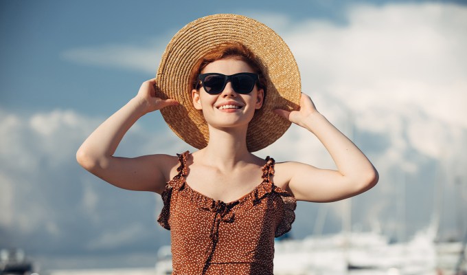 poses for pictures: woman wearing sunglasses grabs the brim of her sunhat