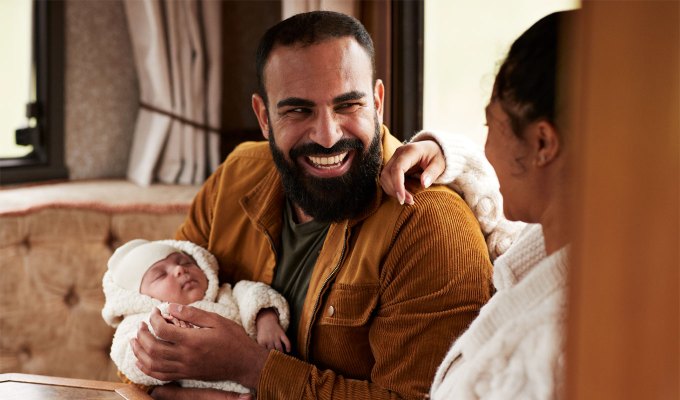questions-for-couples: Happy father laughing while carrying baby daughter and looking at mother in camper van. The man appears to be Middle Eastern.