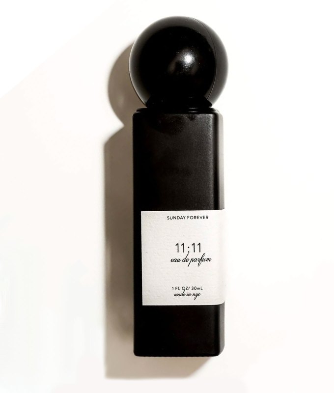 bedtime-perfume-trend: A black minimalist type of perfume bottle from Sunday Forever. It's rectangular with a spherical cap and a white label. It sits in front of a white background.